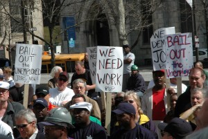 Unemployed workers march carrying signs that say "We Need Work"