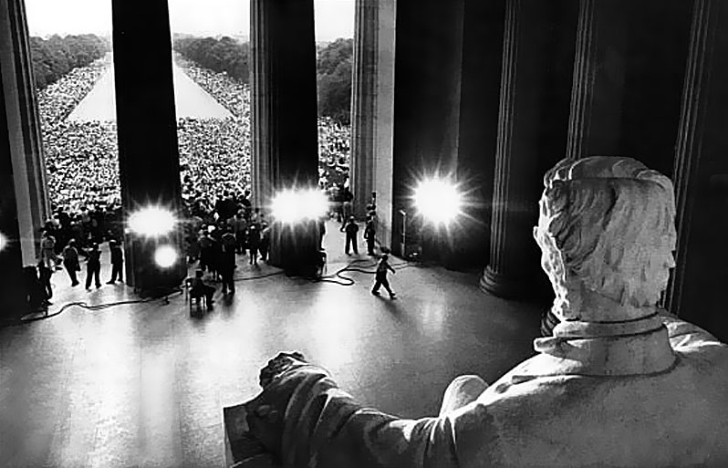glack and white photo of the crowd at MLK I have a dream speech shot from behind the statue of Abraham Lincoln's head in the Lincoln Memorial